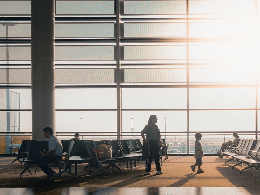 An airport departure lounge, with a parent and child standing by the windows in the afternoon light